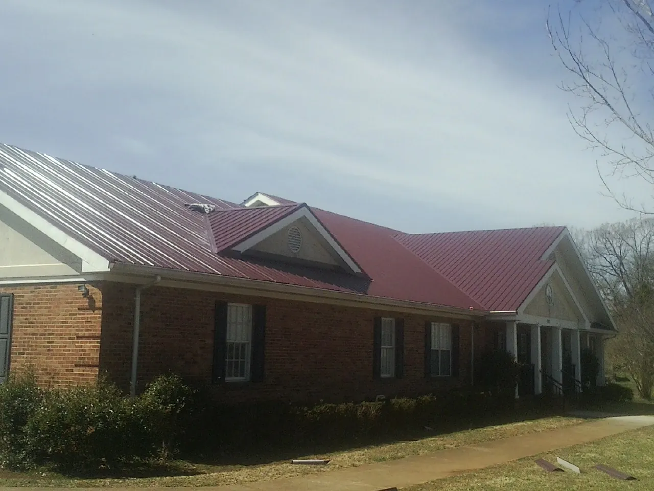 Red metal roof with gabled entries on a long brick building, from a Hail Damage Roof Repair job in Pittsburgh