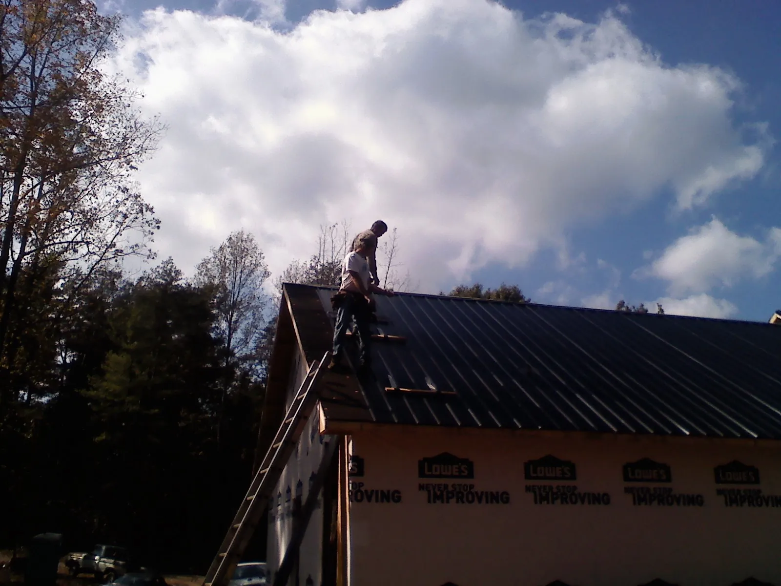 Roofer fastening dark metal panels high against a cloudy sky, from a Roof Inspection job in Pittsburgh