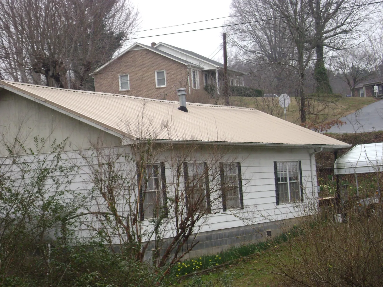 Tan metal roof on a white sided house set into a hillside — Commercial Roofing by Roofing Brothers in Pittsburgh